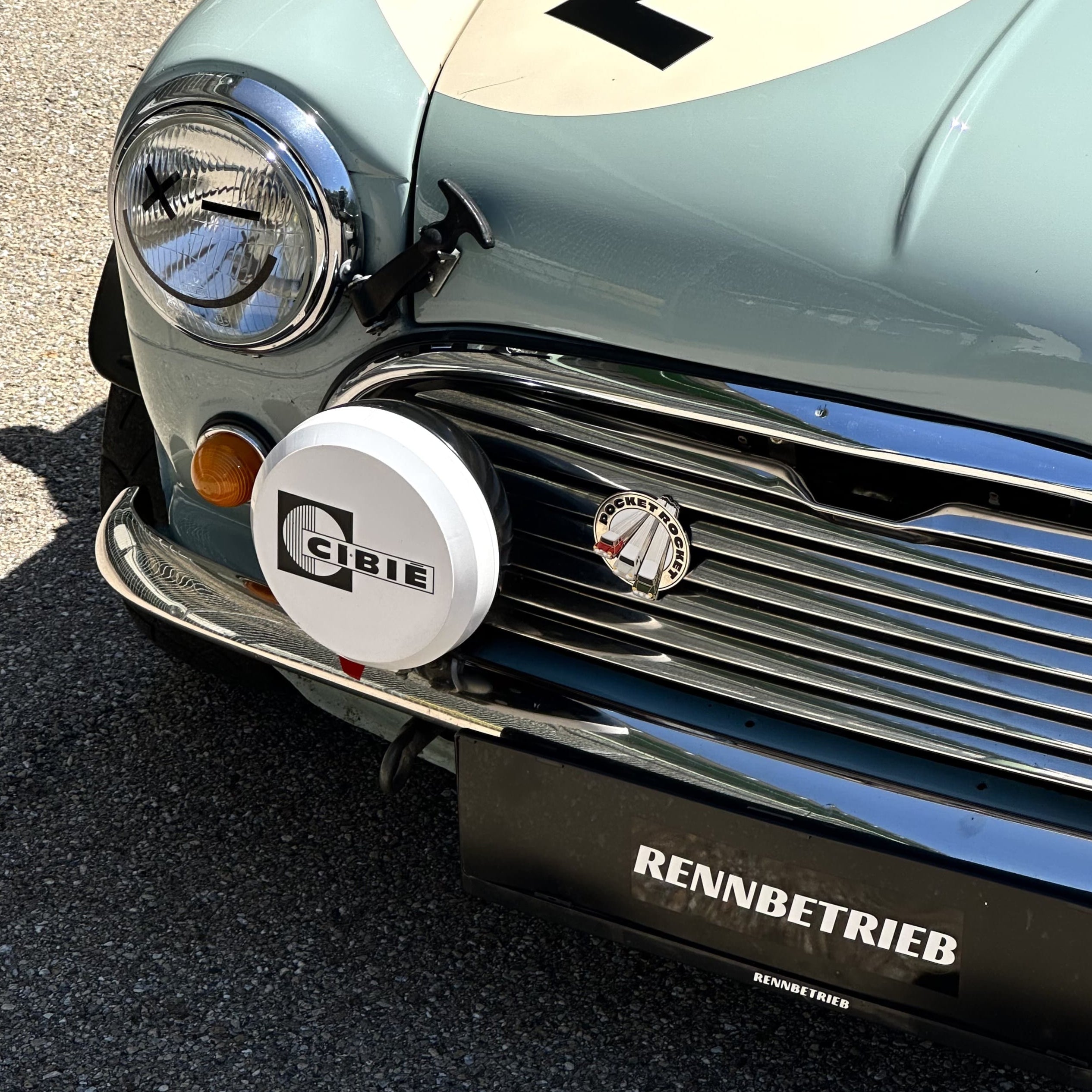 mini cooper car with number 72 on the hood, parked on a gravel surface.