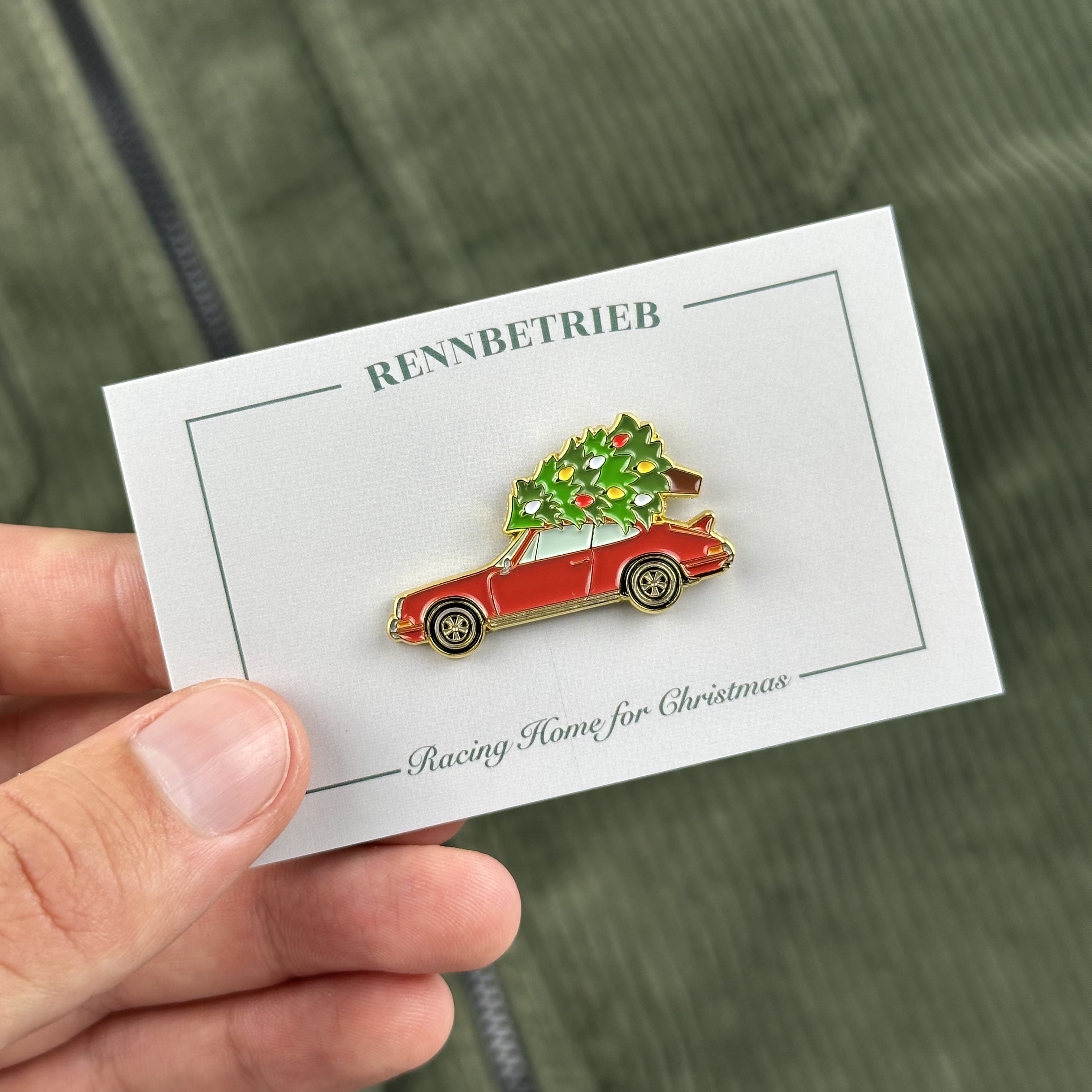 Pin of a red car with a Christmas tree on a card held by a hand.