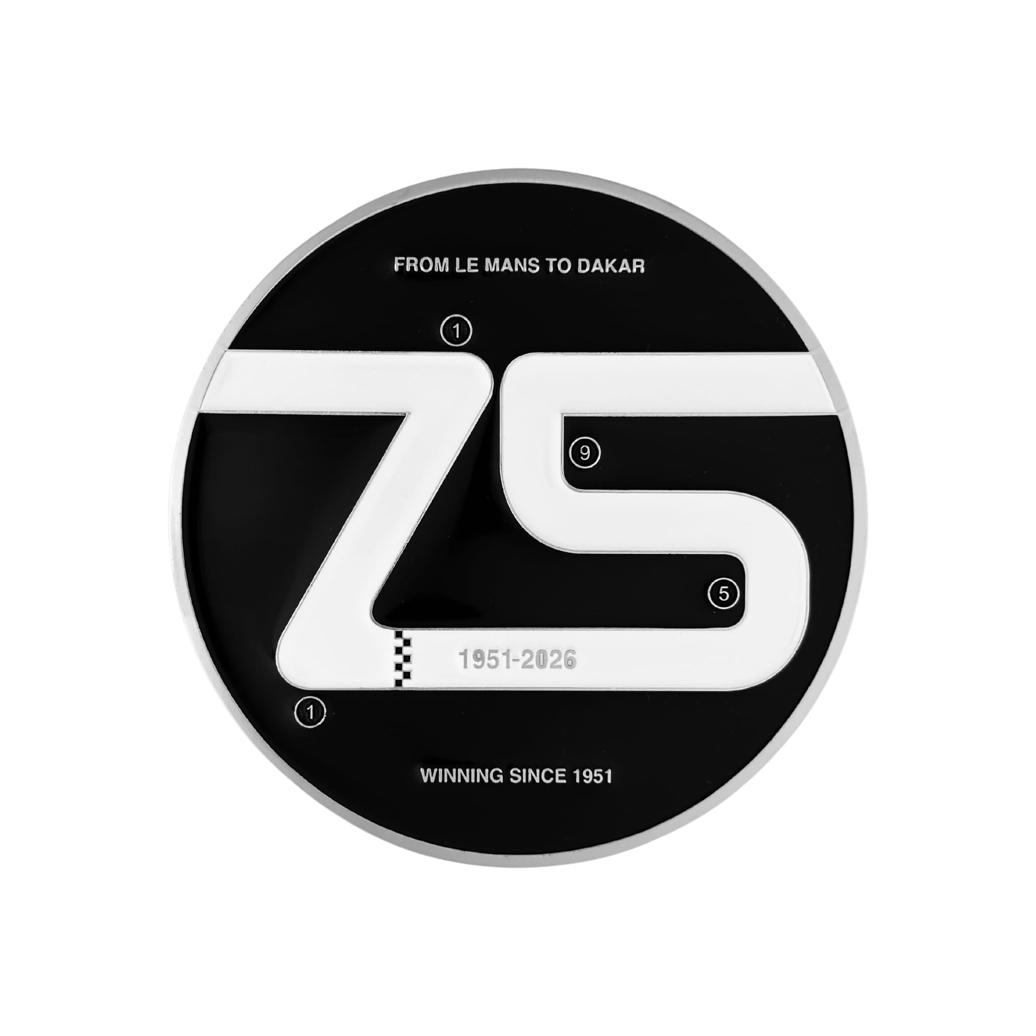 A round commemorative plaque celebrating 75 years of motorsport, featuring a black and white design with the number 75, track layout elements, and text reading 'FROM LE MANS TO DAKAR' and 'WINNING SINCE 1951'.