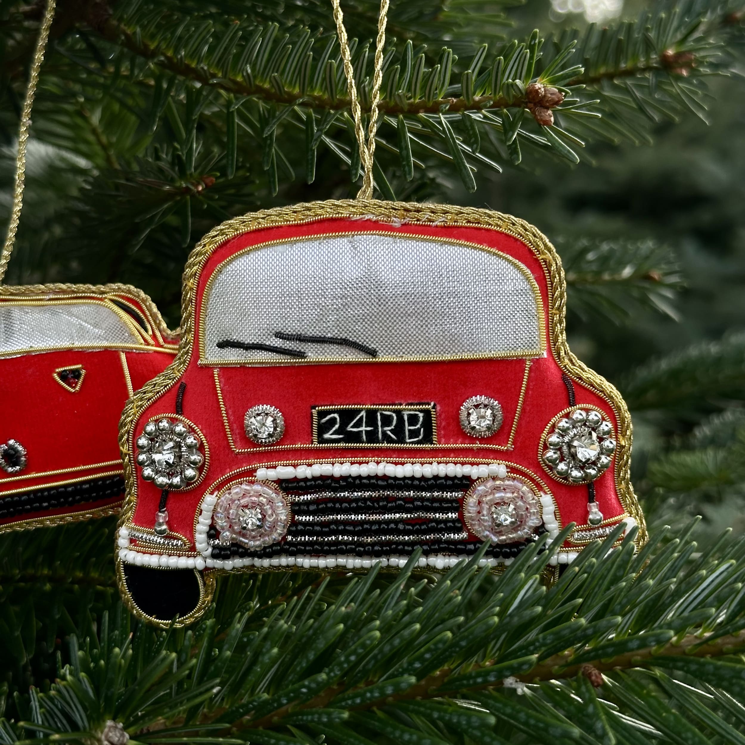 Decorative red car ornaments with gold accents hanging on a Christmas tree.